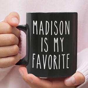 May include: Black coffee mug with white text that reads "MADISON IS MY FAVORITE".