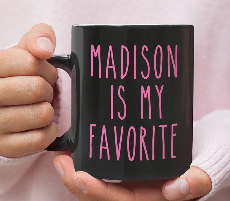 May include: Black coffee mug with a pink inscription that reads "MADISON IS MY FAVORITE".