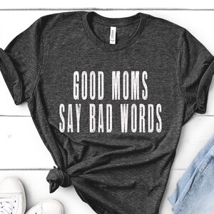 May include: A dark grey t-shirt with the text "GOOD MOMS SAY BAD WORDS" printed in white.