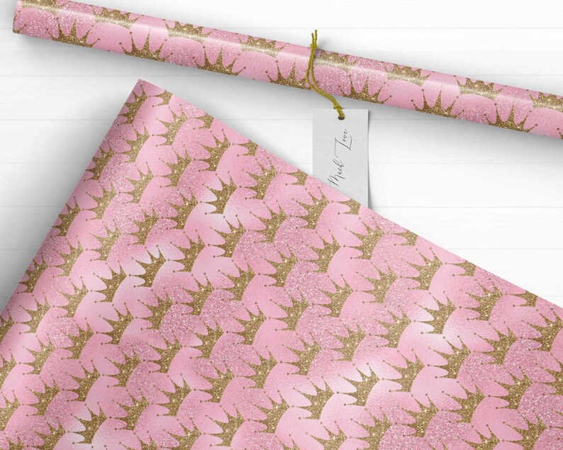 May include: Pink wrapping paper with a repeating pattern of gold glitter crowns. The paper has a subtle shimmer.