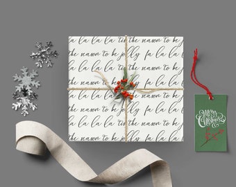 May include: White gift wrap with the text "la la la la tis the season to be the reason to be jolly fa la la la la la la tis the season to be the season to be jolly fa la la la la la la tis the season to be the reason to be jolly fa la la la" repeated. A green gift tag with the text "Merry Christmas" in white cursive is attached to the gift wrap with red string.