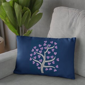 Puede incluir: Una almohada azul marino con un &aacute;rbol blanco bordado con corazones morados.