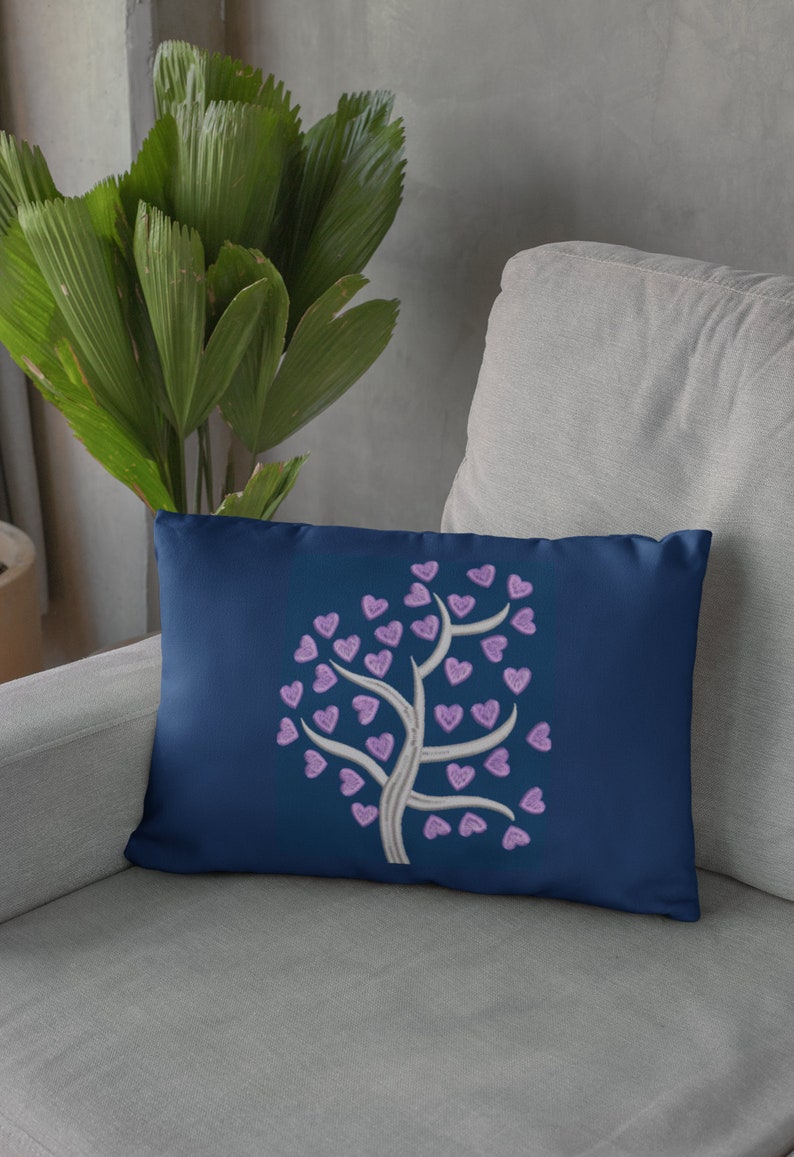 Puede incluir: Una almohada azul marino con un &aacute;rbol blanco bordado con corazones morados.