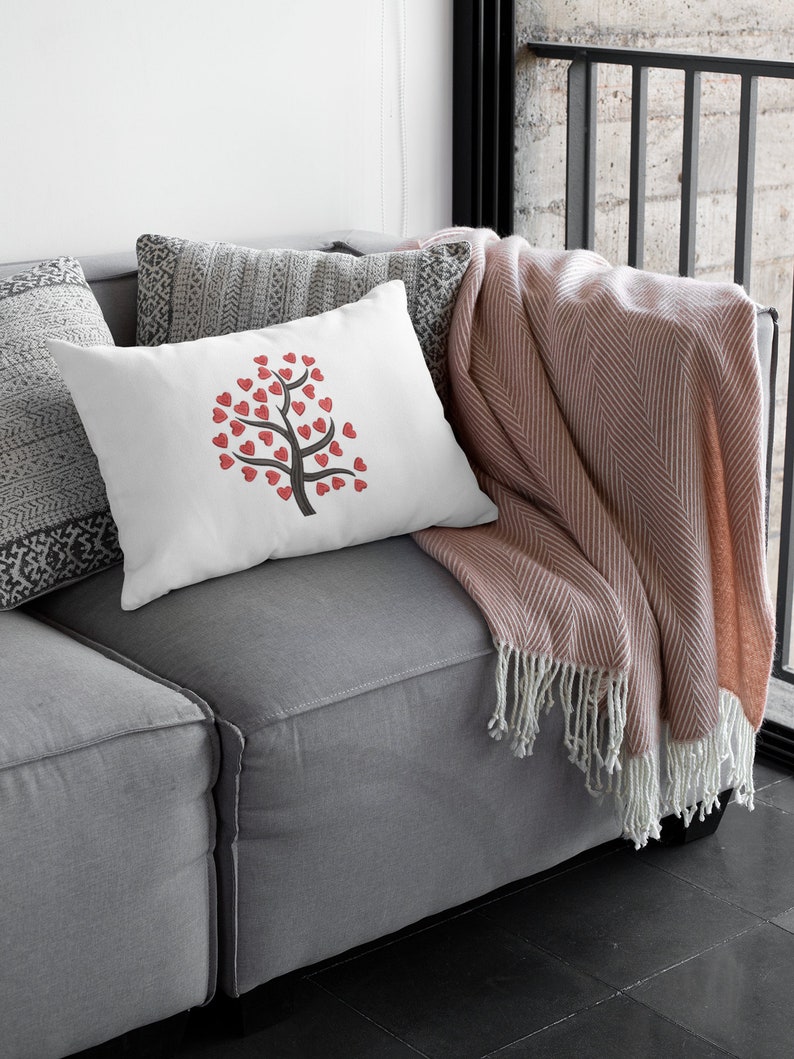 Puede incluir: Una almohada blanca con un dise&ntilde;o de &aacute;rbol de corazones rojos en un sof&aacute; gris con una manta de color rosa.