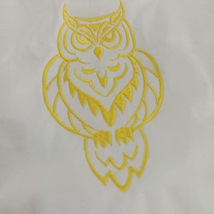 Puede incluir: Un dise&ntilde;o de b&uacute;ho bordado en amarillo sobre un fondo de tela blanco.