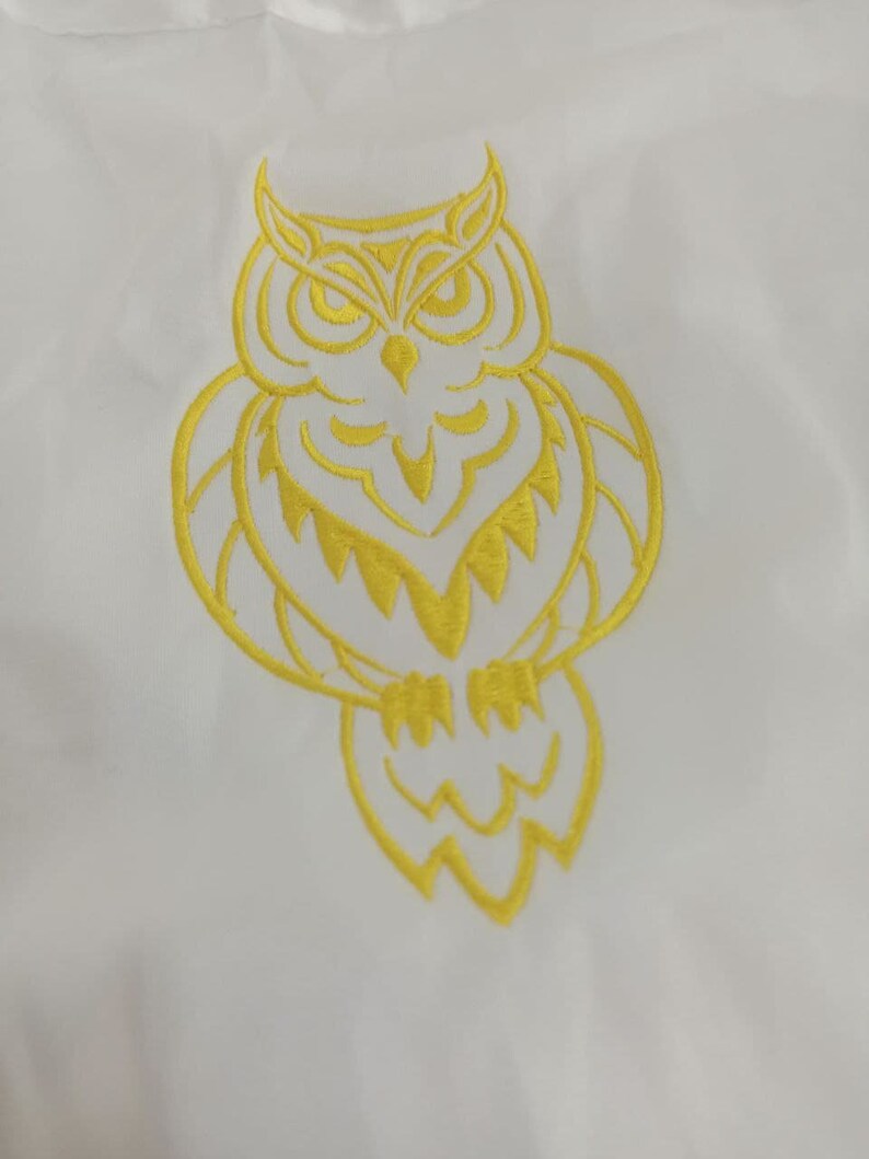 Puede incluir: Un dise&ntilde;o de b&uacute;ho bordado en amarillo sobre un fondo de tela blanco.