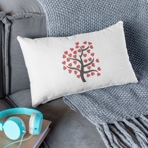 Puede incluir: Una almohada blanca con un dise&ntilde;o de &aacute;rbol de corazones rojos en un sof&aacute; gris con una manta gris.