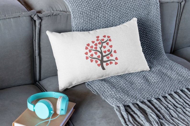 Puede incluir: Una almohada blanca con un dise&ntilde;o de &aacute;rbol de corazones rojos en un sof&aacute; gris con una manta gris.