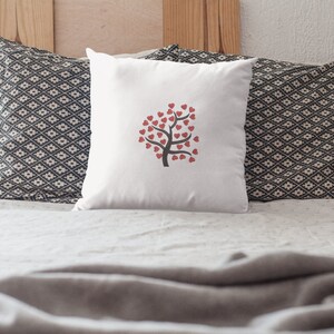Puede incluir: Almohada blanca con un dise&ntilde;o de &aacute;rbol de corazones rojos. La almohada est&aacute; sobre una cama con una funda n&oacute;rdica blanca y dos almohadas con estampado blanco y negro.