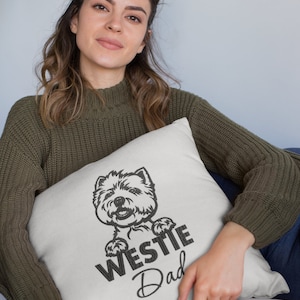 K&ouml;nnte beinhalten: Ein wei&szlig;es Kissen mit einer schwarz-wei&szlig;en Illustration eines Westie-Hundes, der &uuml;ber den Rand schaut. Der Text "Westie Dad" ist unter dem Hund gedruckt.