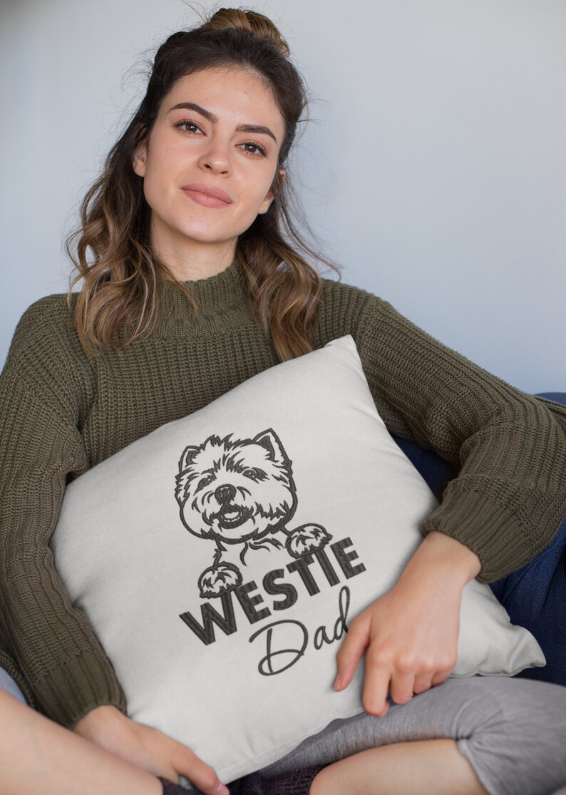 K&ouml;nnte beinhalten: Ein wei&szlig;es Kissen mit einer schwarz-wei&szlig;en Illustration eines Westie-Hundes, der &uuml;ber den Rand schaut. Der Text "Westie Dad" ist unter dem Hund gedruckt.
