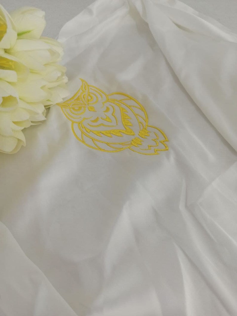 Puede incluir: Tela blanca con un dise&ntilde;o de b&uacute;ho bordado en amarillo.