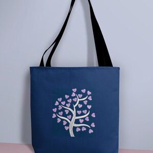 Puede incluir: Una bolsa de tela azul marino con un dise&ntilde;o de &aacute;rbol blanco con corazones rosas para las hojas.