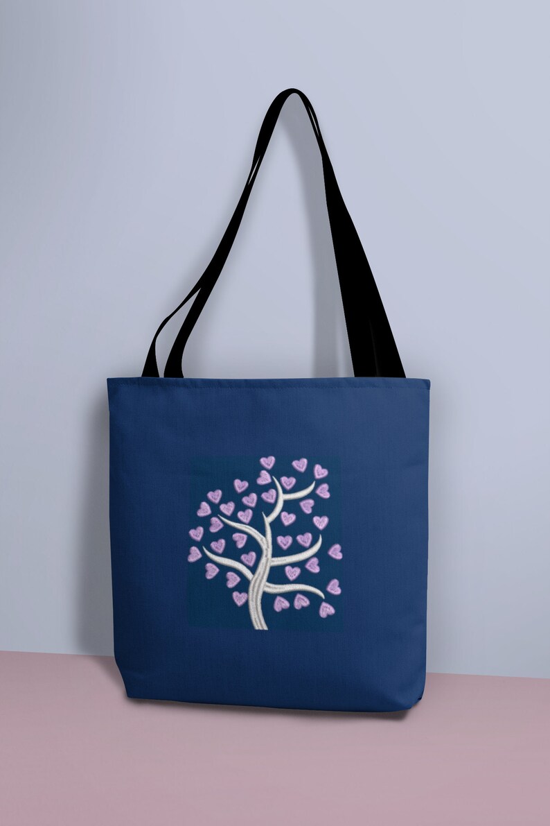 Puede incluir: Una bolsa de tela azul marino con un dise&ntilde;o de &aacute;rbol blanco con corazones rosas para las hojas.