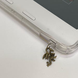 May include: A gold-colored dragon charm attached to a clear phone case.
