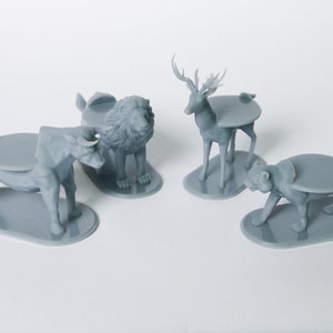 May include: Four gray 3D printed animal figurines with round bases. The animals are a bull, a lion, a deer, and a tiger.