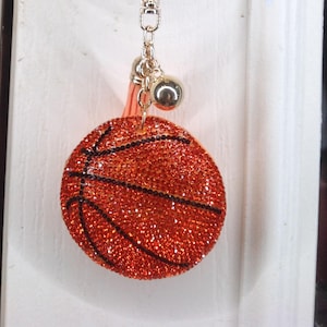 Może przedstawiać: Złoty klamka drzwi z łańcuchem przymocowanym do błyszczącego pomarańczowego breloka w kształcie piłki do koszykówki.