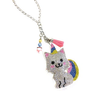 May include: A silver chain with a pink tassel and a rhinestone unicorn charm. The unicorn is white with a pink, blue, and yellow mane and tail.