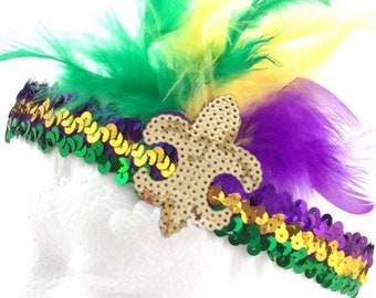 May include: A Mardi Gras headband with green, purple, and gold feathers and sequins. A gold fleur-de-lis charm is attached to the headband.