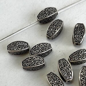May include: A group of silver-toned metal beads with a floral design. The beads are oval shaped and have a raised floral pattern.