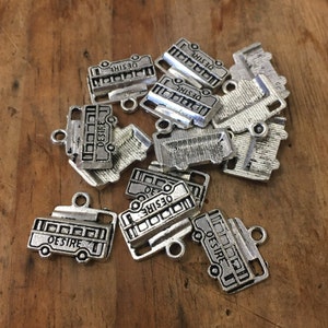 May include: A group of silver-toned metal charms shaped like school buses. Each charm has the word "DESIRE" printed on it.