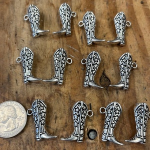 May include: Twelve silver cowboy boot charms with a star pattern. The charms have a loop at the top for attaching to a necklace, bracelet, or keychain.
