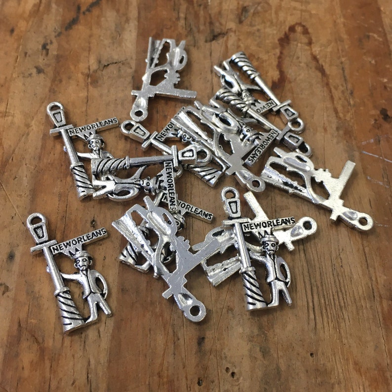 May include: A collection of silver charms featuring a cartoon figure holding a street sign that reads "New Orleans". The charms are in various positions and some are partially obscured by others.