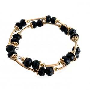 May include: A gold bracelet with black faceted beads. The bracelet is made of two thin gold wires that are wrapped around each other.