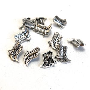 May include: A collection of silver-toned metal cowboy boot buttons. The buttons are detailed with a boot design and have a flat back.