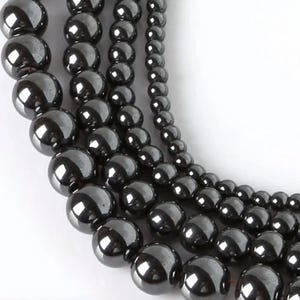 Op de afbeelding: Een streng zwarte hematiet kralen in verschillende maten. De kralen zijn rond en hebben een gladde, gepolijste afwerking.