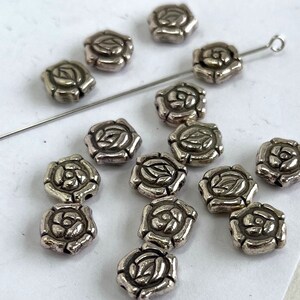 May include: A collection of silver-toned metal beads with a rose design. The beads are scattered on a white surface.