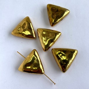 May include: Five gold-colored triangle-shaped beads with a textured surface. The beads have a hole in the center for stringing.