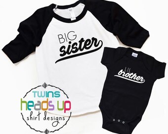 Puede incluir: Una camiseta blanca y negra de estilo béisbol con las palabras "BIG sister" en escritura negra. Un body negro con las palabras "lil brother" en escritura blanca. Las camisas forman parte de un conjunto. También es visible el logotipo "Twins Heads Up Shirt Designs".