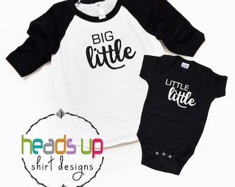 Puede incluir: Una camiseta blanca y negra de estilo béisbol con las palabras "BIG little" en escritura negra. También se muestra un body negro con las palabras "LITTLE little" en escritura blanca. Las camisetas son de "heads up shirt designs".