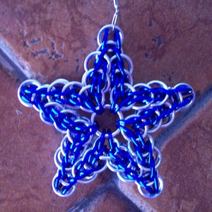 Puede incluir: Un adorno en forma de estrella azul y plateado hecho de malla de cadena.