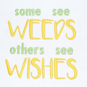 May include: A white background with the text "some see weeds others see wishes" in yellow and green embroidery.