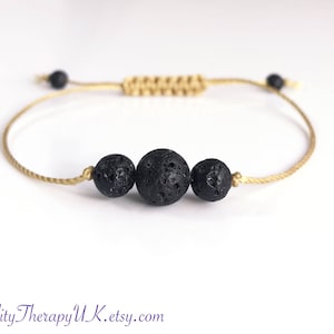 May include: A simple bracelet made with a beige cord and three black lava rock beads.