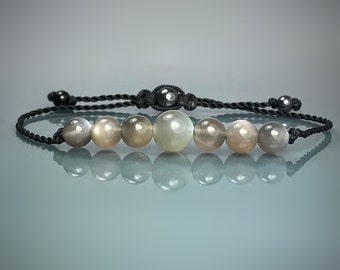 May include: A black cord bracelet with seven light gray moonstone beads and black hematite beads at each end.