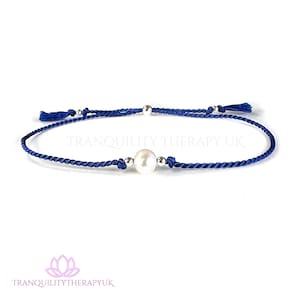 May include: A blue string bracelet with a white pearl and silver beads. The bracelet is tied with a knot and has tassels on each end. "Tranquility Therapy UK" is printed on the white background.