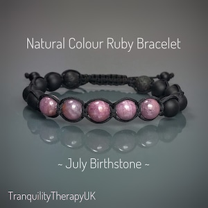 May include: A black cord bracelet with pink ruby beads and black lava beads. The bracelet is tied with a knot and has a July birthstone tag. "Natural Colour Ruby Bracelet - July Birthstone - TranquilityTherapyUK" is written on the image.
