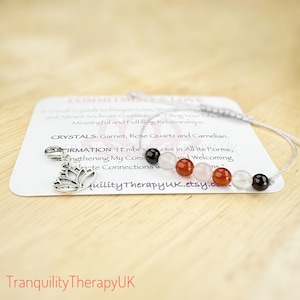 Puede incluir: Un brazalete de plata con un dije de flor de loto y cuatro cuentas de piedras preciosas: granate, cuarzo rosa, cornalina y cuarzo transparente. El brazalete está sobre una tarjeta blanca con el texto "CRYSTALS: Garnet, Rose Quartz and Carnelian. AFFIRMATION: "I Embrace Love in All Its Forms, Strengthening My Connections and Welcoming Infinite Connections w..." y "quilityTherapyUK.etsy.com".
