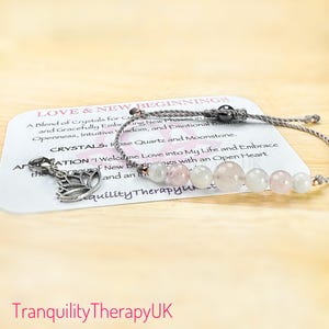 May include: A grey string bracelet with a silver charm and pink and white gemstone beads. The bracelet comes with a card that reads "Love & New Beginnings" and lists the crystals used: Rose Quartz and Moonstone. The card also includes the affirmation "I welcome love into my life and embrace new beginnings with an open heart."