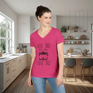 Peut inclure: Un t-shirt magenta à col en V avec le texte "ROCK OUT with your CROCK OUT" et un dessin d'une mijoteuse. Le t-shirt est fait d'une matière douce, adapté pour un usage décontracté.
