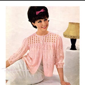 May include: A pink knitted cardigan with a button-up front and a delicate lace pattern. The cardigan has a round neckline and three-quarter sleeves.