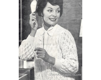 May include: A white knitted cardigan with a cable knit pattern and a button closure. The cardigan has a collar and long sleeves. The model is wearing the cardigan and holding a hairbrush.