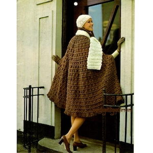May include: A brown crocheted cape with a white crocheted hat and scarf. The cape has a fringe trim and is worn by a woman standing in front of a door.
