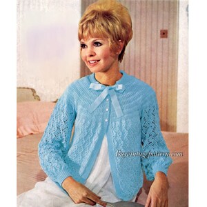 Peut inclure: Un cardigan en tricot bleu clair avec un motif en dentelle et un nœud au niveau du col. Le cardigan est boutonné sur le devant et a des manches longues.