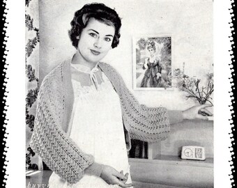 May include: A black and white photograph of a woman wearing a knitted shawl with a lacy pattern. She is standing in a room with a picture on the wall and a clock on a shelf.