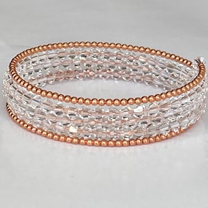 Könnte beinhalten: Ein Armband aus klaren Kristallperlen mit einer Kupferdrahtumwicklung. Das Armband besteht aus mehreren Perlenreihen und hat einen zarten, femininen Look.