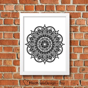 May include: Black and white mandala design print in a white frame against a brick wall background.